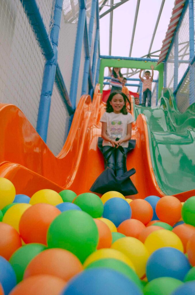 Playground naranja con piscina de pelotas inferior, niña sonriendo